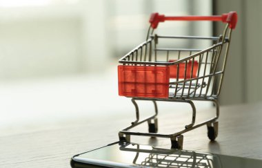 Ahşap yüzeydeki alışveriş arabasını ve cep telefonunu kapat. Para harcamaları ve mali geçmiş kavramı