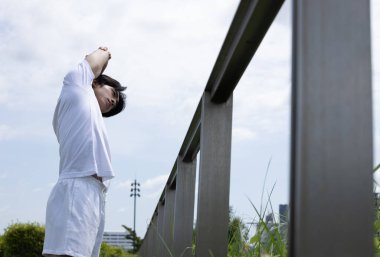 Beyaz tişörtlü Asyalı genç adam parkta uzanıyor. Parkta sağlık yaşam tarzı kavramı.