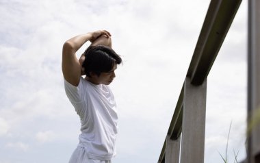 Beyaz tişörtlü Asyalı genç adam parkta uzanıyor. Parkta sağlık yaşam tarzı kavramı.