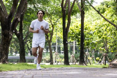 Parkta koşan beyaz gömlekli Asyalı yakışıklı adam. Parkta sağlık yaşam tarzı kavramı.