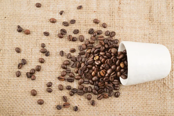 Cup full of coffee beans over hessian cloth — Stock Photo, Image