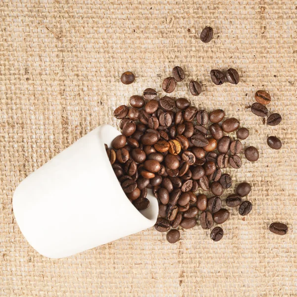 Copo cheio de grãos de café sobre pano hessiano — Fotografia de Stock