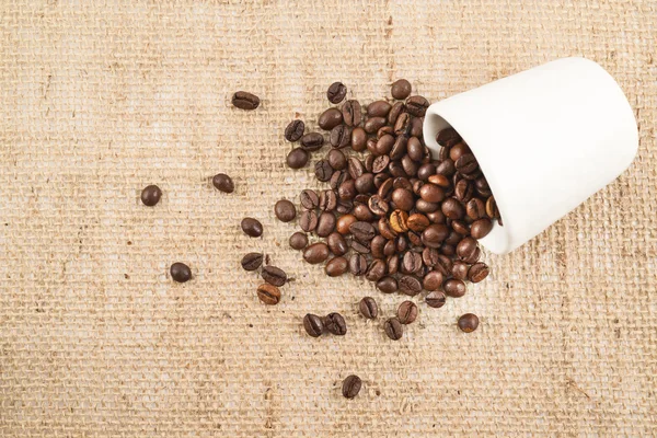 Copo cheio de grãos de café sobre pano hessiano — Fotografia de Stock