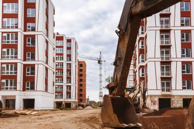 Vinçlerle inşa ediliyor. İnşaat alanında kazıcı. Şehrin arka planında yeni bir ev. çok renkli evler.