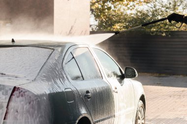 Araba, dışarıdaki otomatik lavabodaki bir hortumun güçlü su basıncının altında yıkanıyor. Araba temizleme kavramı.