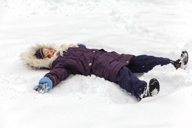 Kışlık giysili ve su geçirmez eldivenli kış çocuğu. Karda yatan küçük kız. Karlı oyun oynuyor. Kış yürüyüşü.