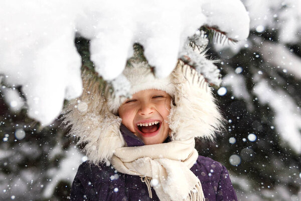 Winter child portrait. Positive smiling adorable little girl face in snow park in snowfall. Winter active walking