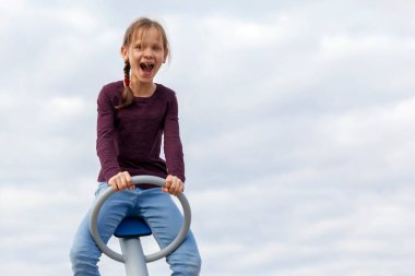 Sallan Çocuk. Sevimli küçük kız mutlu bir şekilde gülüyor, arka planda salıncakta sallanıyor. Mutluluk, özgürlük, keyif, sağlık. 