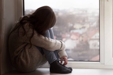 Depresyonda olan genç, pencerenin kenarında tek başına oturuyor. Üzgün Genç 'in yardıma ihtiyacı var. Gençlik sorunları. Olumsuz düşünce. İçe dönük
