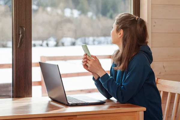 Serbest çalışan biri. Genç bir kadın Laptop bilgisayarı kullanıyor ve çalışıyor, cep telefonu kuzeyde. Pencerenin dışında kış karı.