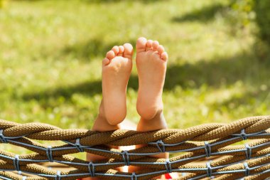 Yaz Tatili, Tatil, Seyahat ve Çocuk kavramı - Hamakta Çıplak Ayaklı Çocuk, güneşli bir günde yeşil doğa arka planında. Mutlu yaz çocukluğu.