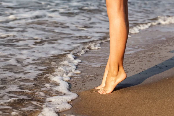 ビーチ旅行の女の子砂の中に波の演奏砂のビーチを歩く 砂浜の砂の上の足日没 — ストック写真