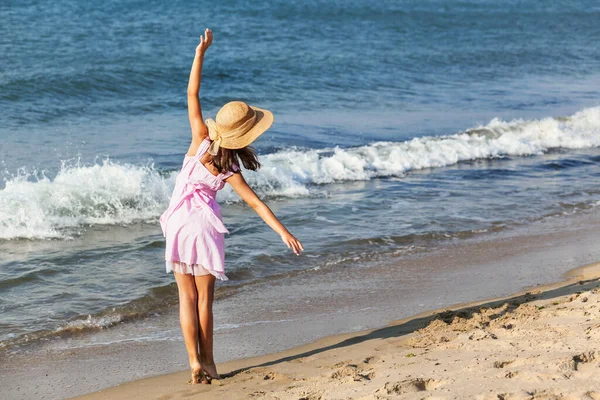 Sea walk along coast. Holidays at sea. Graceful girl in sun hat stand dancing on sea beach.