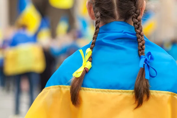 Rally support Ukraine in Europe. Ukrainian Flag on Shoulders of Girl with blue yellow ribbons on flags background.