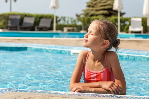 Swimming Pool on Sea Hotel. Beautiful Teen Girl enjoying sunbathes in resort pool. Summer sea vacation. Child relaxing on edge of kids pool