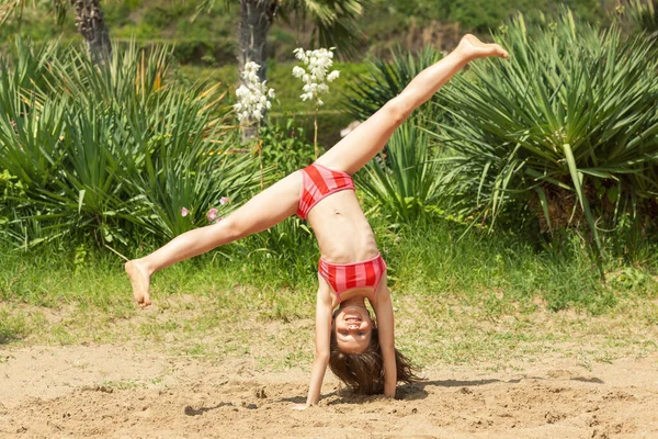 Mutlu Çocuklar Tatili. Güzel Kız Sunny Beach 'te iyi eğlenceler. Neşeli Çocuk Tropikal Sahilde el ele duruyor. Küçük kız Kum 'un üstünde ters duruyor.