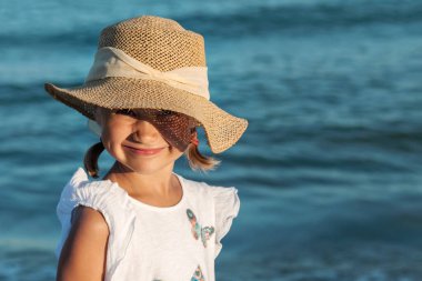 Sea Portrait of Cute Little Girl Child in Sun Hat on Sea Background at Sunset. Sea Kid Face on Blue Sea. Copy space.