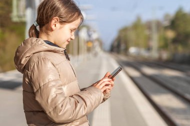 Online Rain ticket booking. Girl uses Mobile Application on Smartphone at Train station. Online Help for Travel. Selective focus