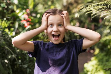 Surprised Girl  not believe such luck. Happy Child with eyes big and open mouth  in Nature Green Background. Shocked Children expression. Adventure leisure concept. 