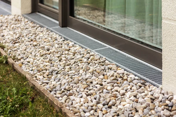 Pebbles for water drainage along perimeter of house. Rainwater harvesting with drainage grid or Drain Grate. 
