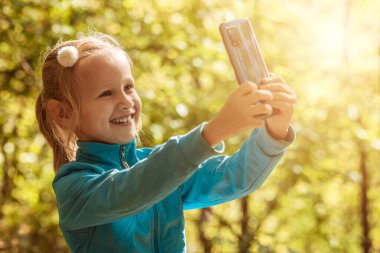 Selfie, çocuğu doğaya taşıyor. Şirin küçük kız parkta selfie çekiyor.