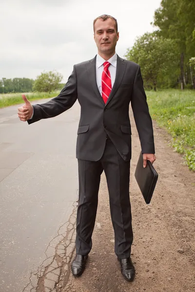Businessman hitchhiking on a road — Stock Photo, Image