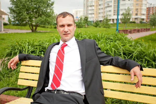 Mladý muž v obleku, sedí na lavičce — Stock fotografie