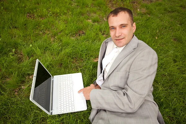 Empresario acostado sobre hierba verde, usando un portátil — Foto de Stock
