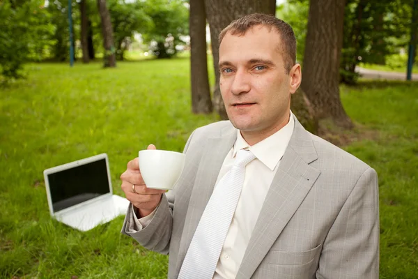 Empresario trabajando en el portátil al aire libre y bebiendo una taza de café — Foto de Stock