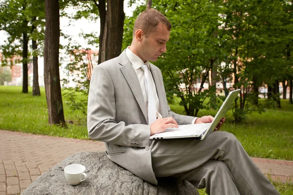 Empresario trabajando en el portátil al aire libre y bebiendo una taza de café — Foto de Stock