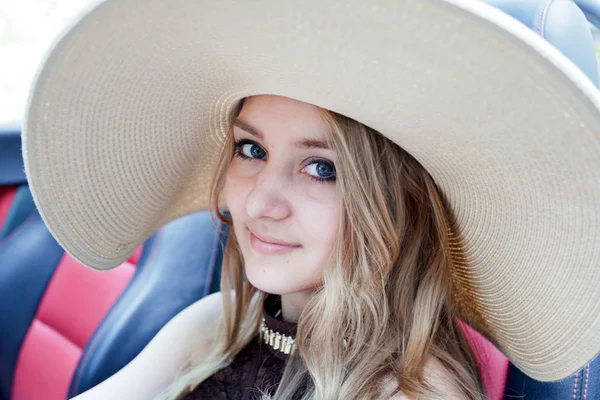 Beautiful woman in a wide brimmed hat sitting in a car — Stock Photo, Image