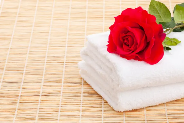 Стопка белого полотенца с красной розой на бамбуковом столе — стоковое фото