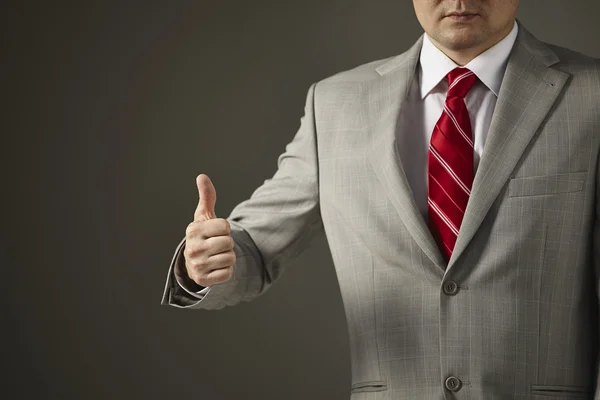 Businessman in a gray suit shows the hand symbol of success — Stock Photo, Image