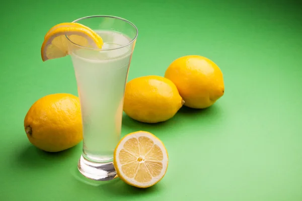 Glas Wasser und frische Zitrone auf grünem Hintergrund — Stockfoto