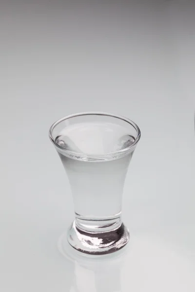 灰色の背景上に分離されてアルコールで満たされた小さなショット グラス — ストック写真
