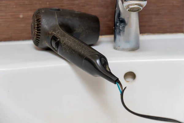 Alambre eléctrico dañado de un secador de pelo viejo. Secador de pelo viejo en el lavabo en el baño. —  Fotos de Stock
