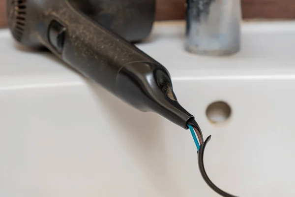 Alambre eléctrico dañado primer plano de un secador de pelo viejo. Secador de pelo viejo en un lavabo en un baño. —  Fotos de Stock