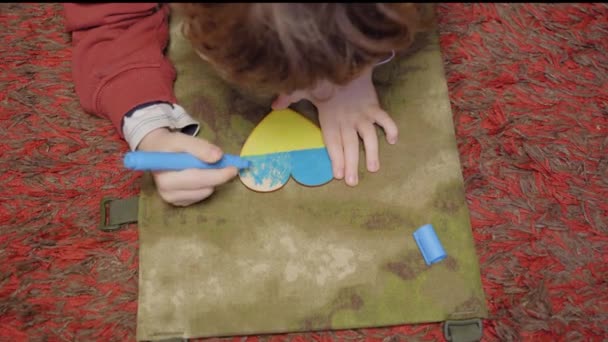 Un enfant peint un cœur aux couleurs du drapeau de l'Ukraine, vue du dessus — Video