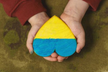 Çocuk elleri Ukrayna bayrağının renklerine boyanmış bir kalbi tutuyor. Yaklaş, üstten bak.