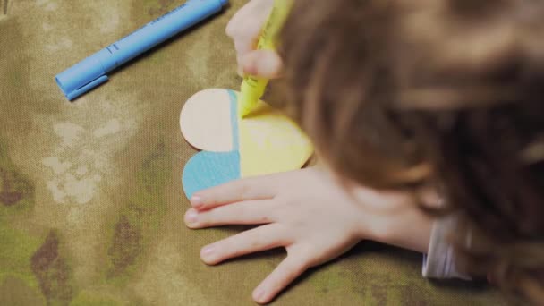 A child paints a heart in the colors of the flag of Ukraine, top view — Stock Video