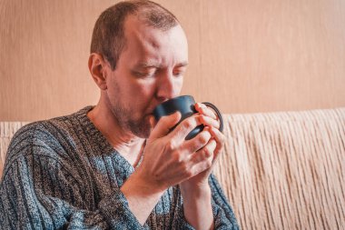 Siyah bardaktan içen bir adamın portresi. Beyaz adam kanepede oturuyor ve yakın plan bir bardaktan içiyor..