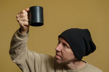 Komik bir genç adam şaşkınlıkla ters dönmüş siyah bir fincana bakar. Siyah şapkalı bir Avrupalının portresi.