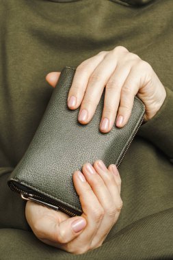 Hands of a girl in a green hoodie close-up, a green purse in her hands.
