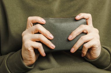 Hands of a girl in a green hoodie close-up, a green purse in her hands