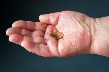 Yaşlı bir kadının elinde bir euro para, gri arka plan, yakın plan..