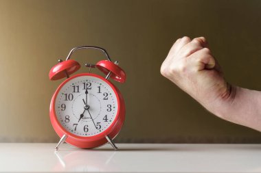 Sabah uyanışı. Kırmızı alarmlı saat. Okları güneşte 7 derece kilitlenmiş ve bir adamın yumruğu yakın plan..