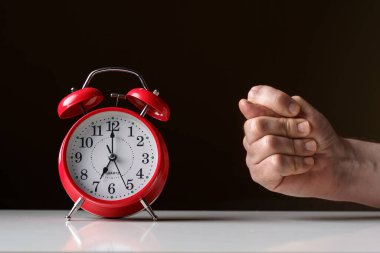 Sabah uyanışı. Saat yedide güneş ışınlarında okları olan kırmızı çalar saat ve bir el incir işareti gösteriyor.