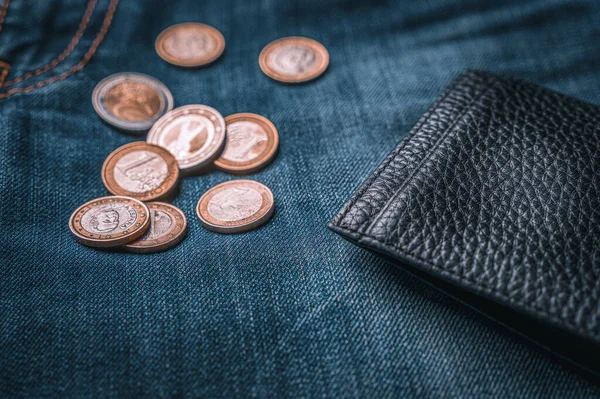 Empty black leather wallet and euro coins on jeans, close up