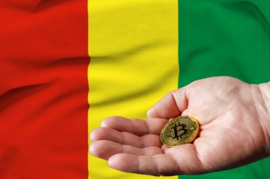 Altın Bitcoin bir adamın elinde, arka planda Gine bayrağı.