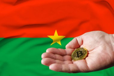 Altın para adamın elinde, Burkina Faso bayrağı da arka planda..